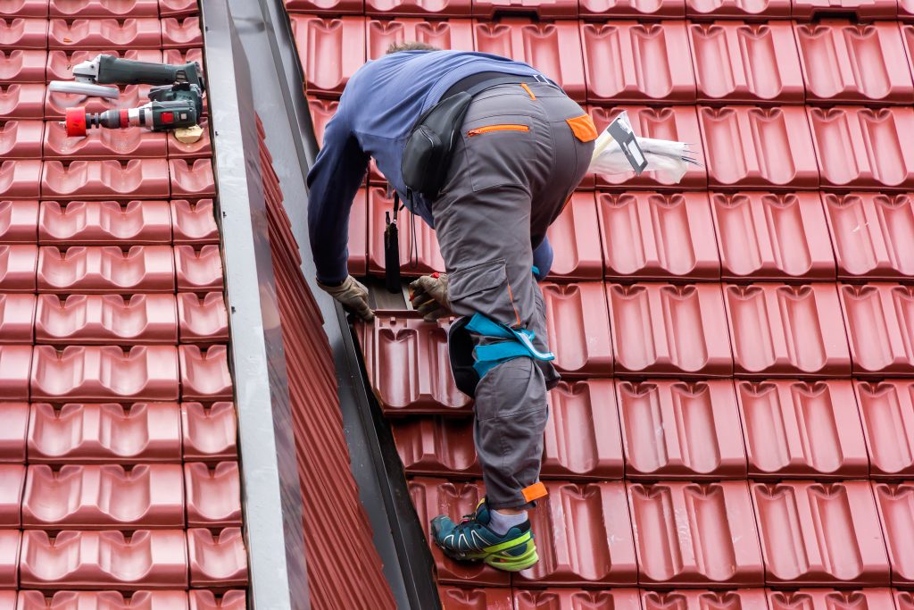 Professional roofer working on house roof with safety gear